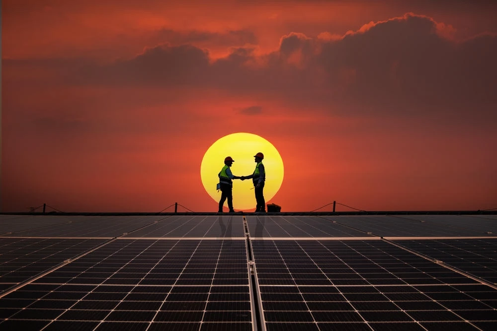 Two installers shaking hands on a solar roof at sunset